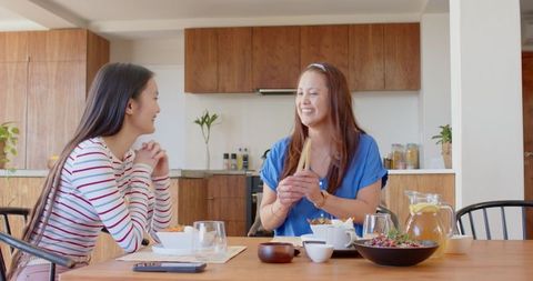 Asian Mother and Daughter Enjoying Meal at Kitchen Table