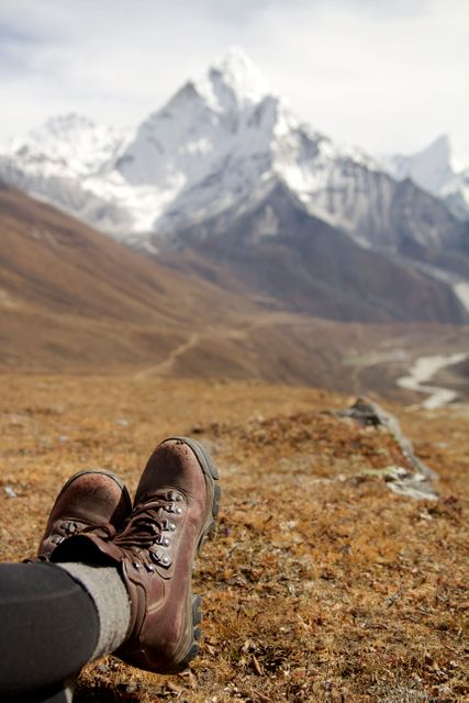 Hiking boots resting on grassy terrain with breathtaking view of snow-capped mountains in background. Ideal for promoting adventure travel, outdoor activities, nature escapes, trekking experiences, hiking gear, and vacation destinations in mountainous regions. Perfect for travel magazines, adventure blogs, and outdoor lifestyle advertisements.