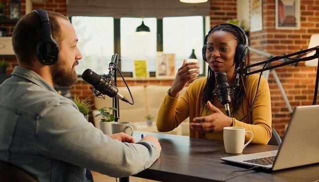 Podcast hosts recording candid interview in cozy brick studio with microphones, headphones