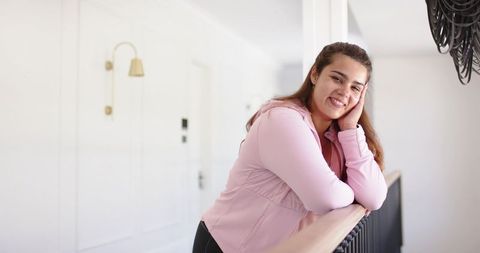 Plus-size woman leaning on railing smiling and resting in bright minimalist home interior