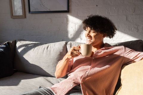 Man relaxing on sunlit sofa holding ceramic mug enjoying cozy morning at home