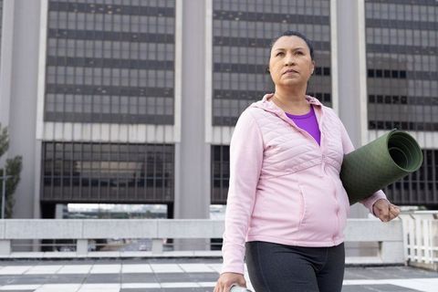 Determined woman holding yoga mat on urban rooftop preparing for outdoor yoga practice