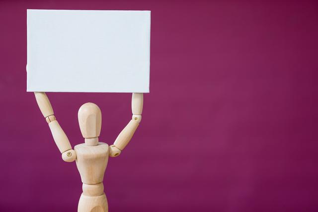 Wooden mannequin holding a blank sign against a purple background. Ideal for use in advertising, marketing, presentations, and communication materials. The empty board provides ample space for custom messages, making it versatile for various concepts such as announcements, protests, or promotional content.