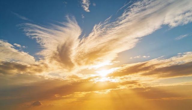 Shining sun illuminating cirrus cloud wings and casting golden sunbeams over dawn horizon