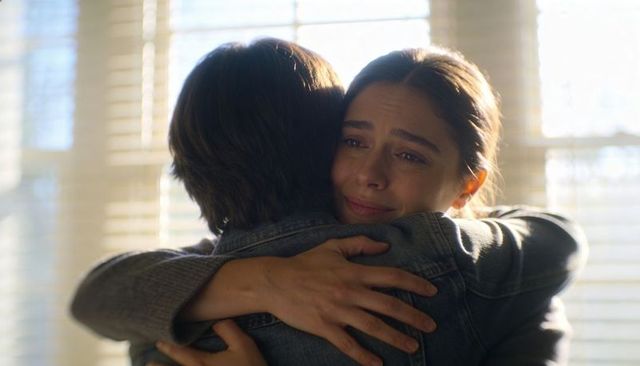 Hugging woman finding comfort during tearful reunion beside sunlit blinds