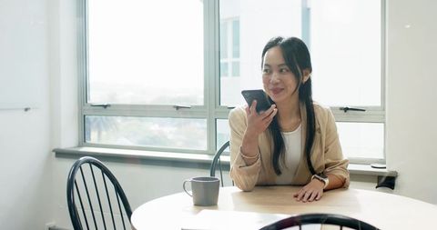 Asian Woman Using Smartphone for Voice Input in Modern Office