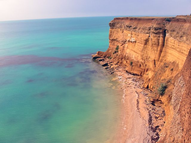 Shows breathtaking aerial view of dramatic sea cliffs with turquoise clear water. Ideal for travel and tourism materials, nature and scenic photos, promoting coastal destinations, and wallpapers depicting serene natural beauty.