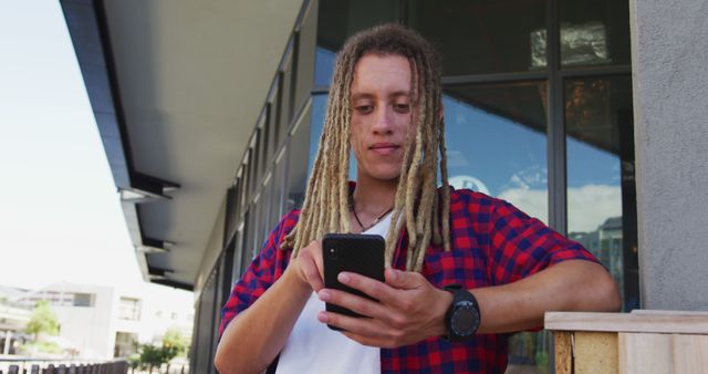 Biracial man with dreadlocks sitting at table outside cafe using smartphone. digital nomad, out and about in the city.