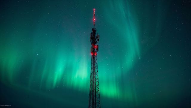 Telecom tower standing under northern lights with red aviation beacons and starry sky