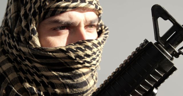 Close-up shows an individual wearing a traditional headdress, partially covering their face, with intense focus on their eyes holding a rifle. Useful for topics related to security, conflict, terrorism, or cultural attire.