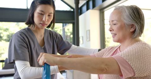 Young Physiotherapist Assisting Senior Asian Woman with Exercise