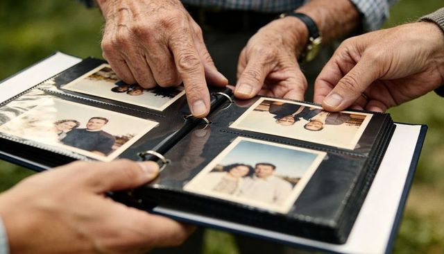 Multigenerational hands turning vintage family album with instant prints outdoors