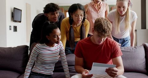 Multicultural friends gathering on sofa, reading letter and reacting to surprising news