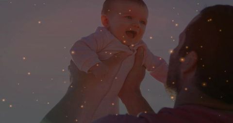 Father lifting baby girl toward sky at sunset with golden dust and joyful laughter