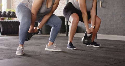 Two women performing kettlebell lifts in industrial gym building strength and teamwork