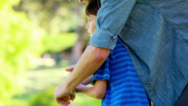 Father coaching his son on how to play baseball in a green park. Man guiding and supporting child with baseball activity. Excellent for concepts of family bonding, sports training, outdoor activities, fatherhood, and physical education. Suitable for advertisements, promotional materials, family-oriented campaigns, and sports lifestyle content.