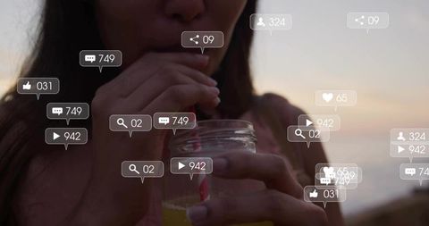 Young woman sipping mason jar drink with striped straw at seaside sunset with social bubbles