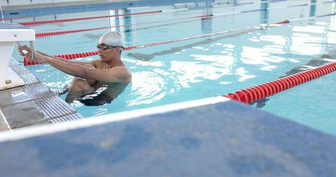Competitive swimmer gripping starting block preparing for backstroke launch in indoor pool