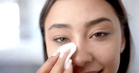 Smiling woman cleansing face with cotton pad for skincare routine