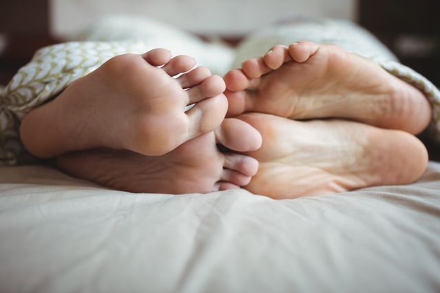 Couple showing their feet while lying on a bed in bedroom