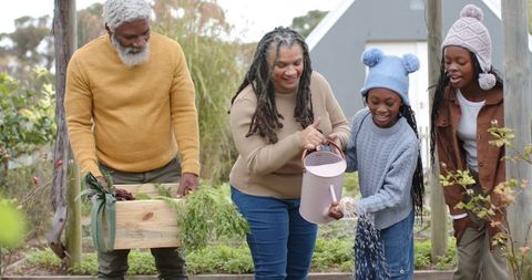 Multigenerational family gardening together in knit sweaters tending raised vegetable beds