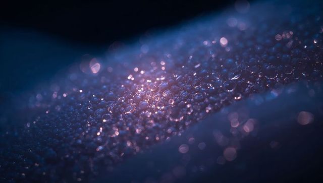 Glittering dew droplets sparkling on leaf producing bokeh and iridescent blue-purple glow