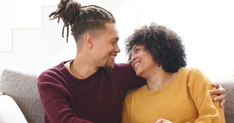 Couple sharing affectionate moment on couch at home, cozy sweaters and bright natural light
