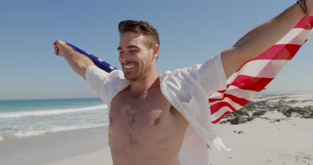 Young Caucasian man celebrates freedom on a sunny beach, with copy space. His joyful expression and the American flag evoke a sense of patriotism and leisure outdoors.