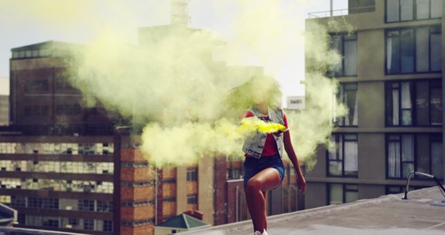 Young biracial woman leaps through yellow smoke on a rooftop. Captured mid-jump, she adds dynamic energy to the urban setting.