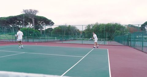Two men playing tennis on outdoor hardcourt near net club match overcast sky