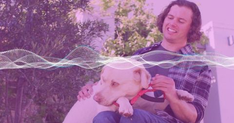Man smiling and adjusting dog collar while holding lab mix companion on garden patio