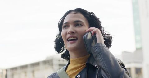 Twenty-something woman talking on smartphone in urban street wearing leather jacket