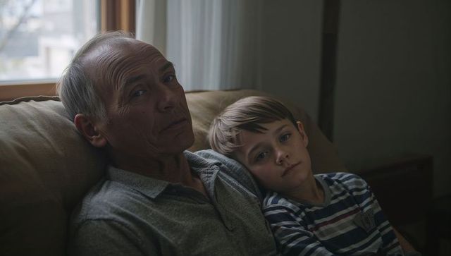 Grandfather Cuddling with Grandson on Sofa During Quiet Afternoon, Intimate Family Moment