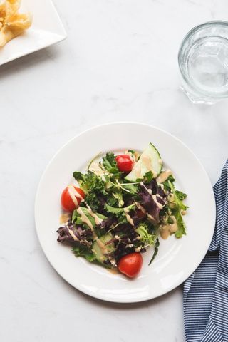 Top-down Mixed Greens Salad Featuring Cherry Tomatoes and Creamy Dressing Drizzling