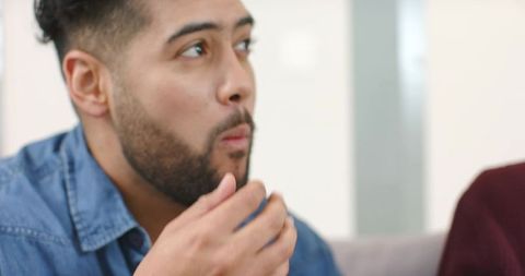 Early-adult man tasting snack on couch during casual home hangout with friend