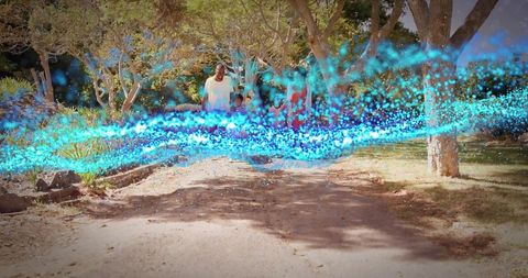 Family Walking Through Sunlit Park With Turquoise Particle Light Trail and Tree Canopy