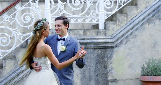 Bride and groom celebrating their wedding day dancing near a vintage staircase. This image can be used for wedding invitations, romance blogs, social media posts featuring love and relationships, or wedding-related advertising.