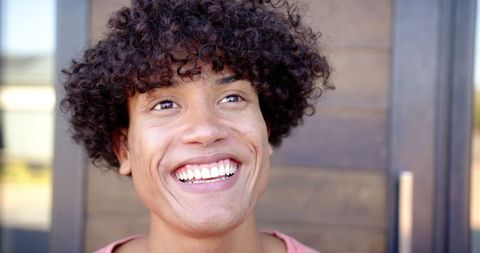 Cheerful Young Man with Curly Hair Smiling Joyfully Outdoors