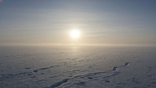 Sunrise glowing over vast sea ice field showing linear cracks and shallow troughs