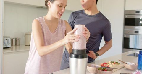 Young couple blending strawberry banana smoothie on modern kitchen island, bright minimal lifestyle