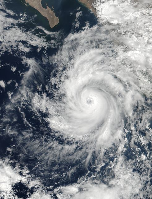 This image shows Hurricane Dora captured from satellite in June 2023, near the Baja California peninsula. The hurricane features a distinct pinhole eye amidst a band of powerful thunderstorms. Ideal for use in weather forecasting publications, educational materials on environmental science, or for news articles covering the impact of natural disasters. Highlights nature's powerful meteorological phenomena and aids in illustrating climate-related courses.