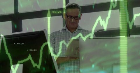 Senior analyst scanning tablet monitoring green stock charts on office monitors