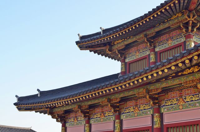 Detailed view of the ornate roofline of a traditional Asian palace, highlighting the intricate designs and vibrant colors against a clear blue sky. Perfect for use in travel articles, cultural heritage projects, and educational materials about Asian architecture and history.