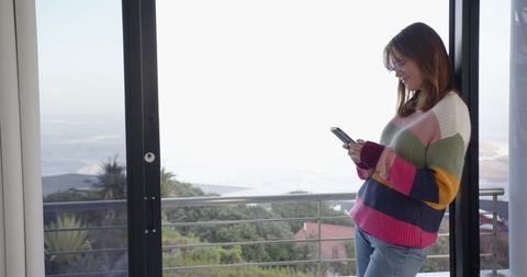 Young woman with smartphone enjoying urban view from balcony