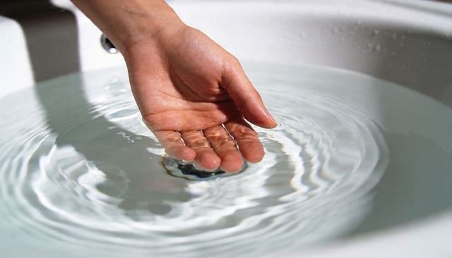 Cupped hand creating circular ripples in white ceramic basin reflecting soft light