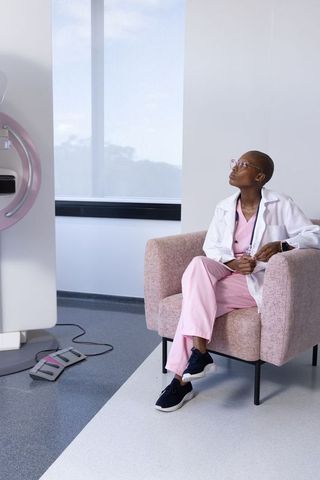 African clinician sitting in pink chair beside medical imaging scanner in modern radiology