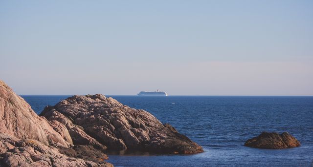 Cruise ship sailing in the distance near a rocky coast under a clear sky. Ideal for travel and tourism promotions, nature blogs, adventure-themed websites, and seascape-related content.
