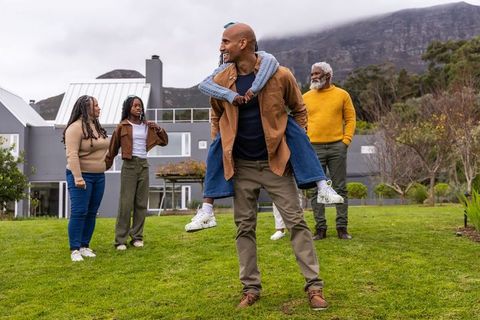 Multigenerational african american family enjoying playful piggyback in front yard with mountain vie