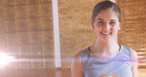 Smiling Teen Girl Holding Basketball in Gym Setting