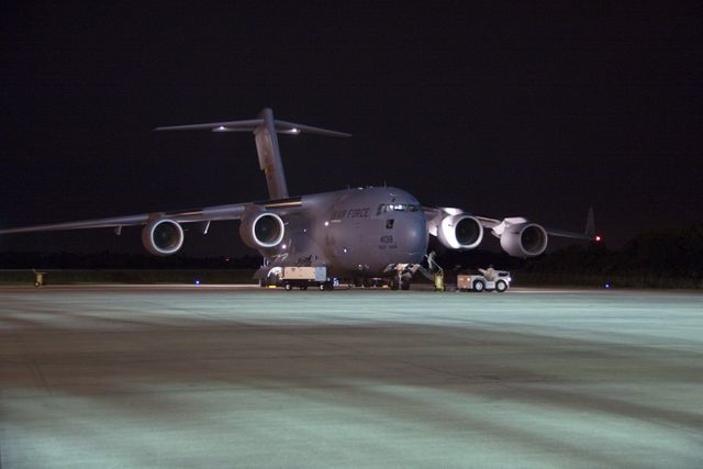 US Air Force C-17 cargo plane stationed at Shuttle Landing Facility at night, unloading equipment for NASA Mars Science Laboratory. Cruise stage, back shell, and heat shield being transferred for processing as part of mission preparations. Useful for articles about aerospace logistics, Mars exploration preparations, and NASA missions.